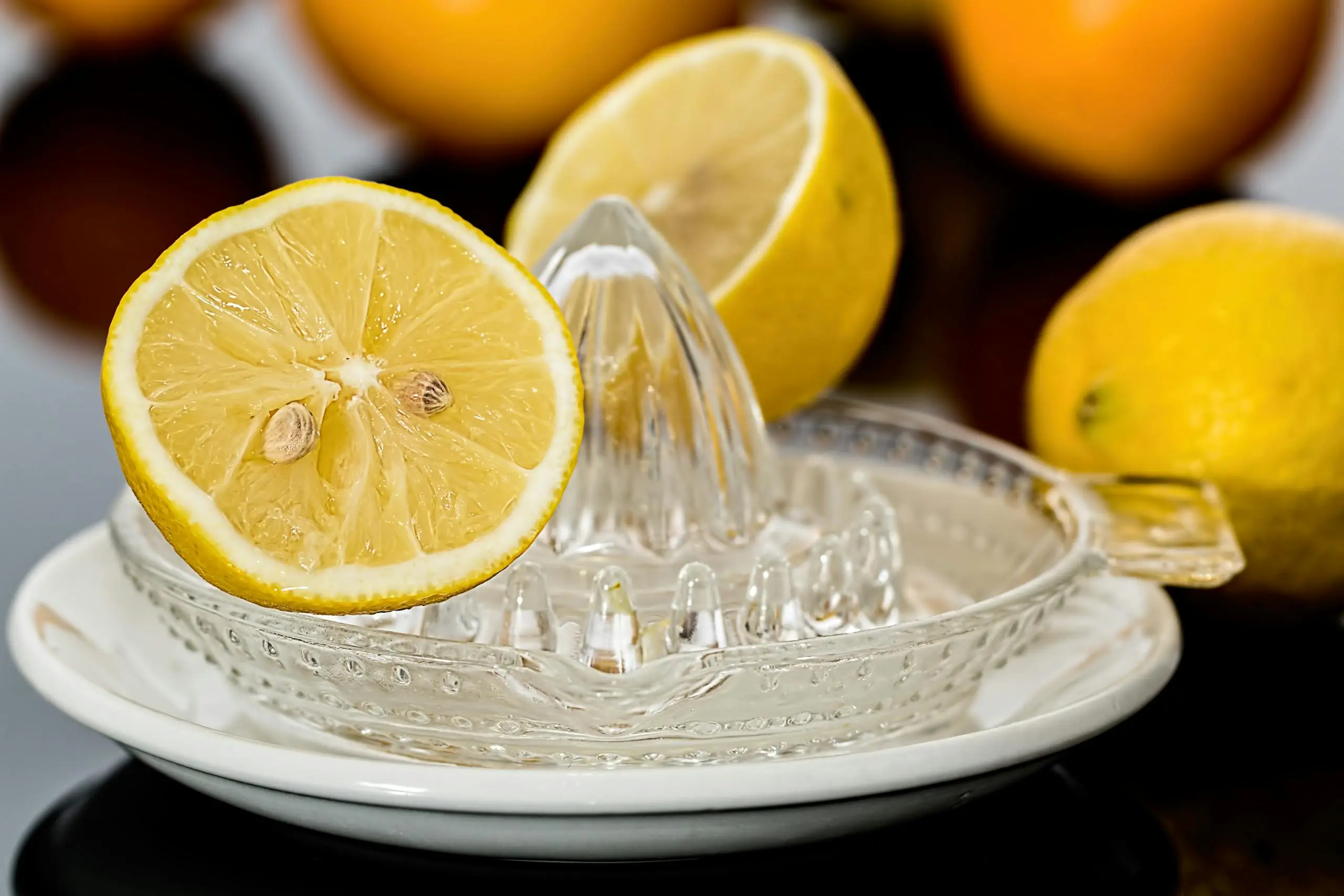 a glass citrus juicer with a halved lemon on top a lemon half in the background and whole lemons nearby Close-up of fresh lemons on a glass juicer ready to make citrus refreshment.